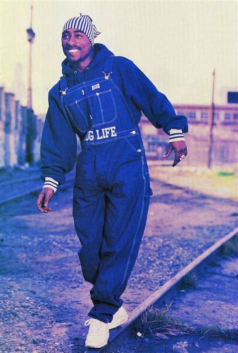 A Man In Blue Jumpsuits Standing On Train Tracks With His Arms Out To