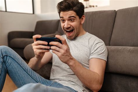Delighted Brunette Guy Playing Video Game On Mobile Phone Stock Photo