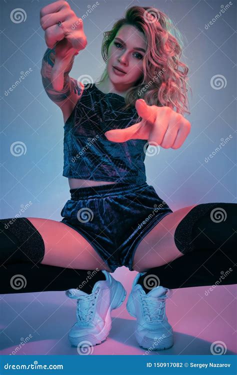 Young Fitness Blonde Woman Wearing Blue Velour Booty Shorts Squats In Front Of Camera Looking
