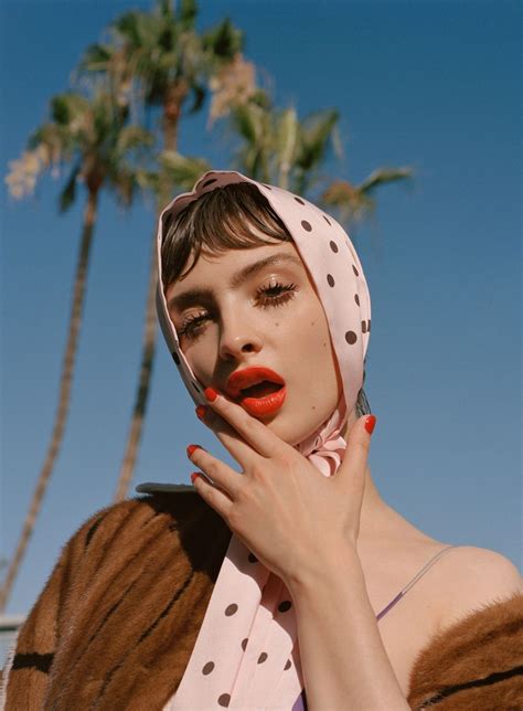 A Woman With Her Hands On Her Face And Palm Trees In The Background Wearing A Polka Dot Scarf