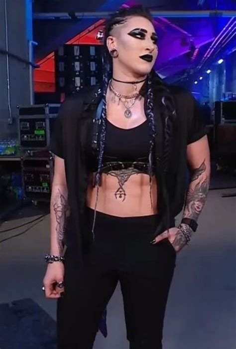A Woman With Black Makeup And Piercings Standing In Front Of A Tv Screen