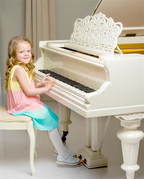 Beautiful Little Girl Is Playing On A White Grand Piano Stock Photo