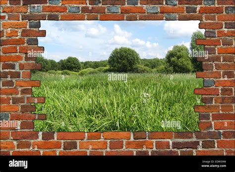 Hole In The Brick Wall And View To Summer Field With Green Grass Stock