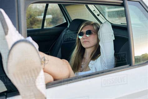 Carefree Female Traveler Resting On Backseat Of Car With Legs Out Of