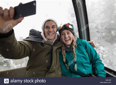 affectionate enthusiastic skier couple riding gondola taking selfie with smart phone stock