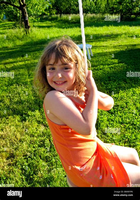 4 year old german girl in orange dress playing on an outdoor swing with a green pasture behind