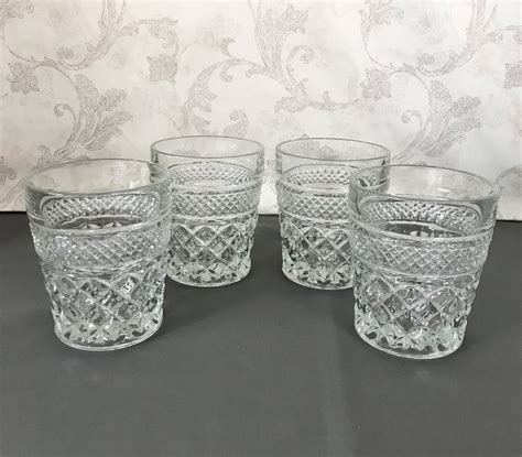 Four Clear Glass Tumblers Sitting Next To Each Other On A Gray Tableclothed Surface