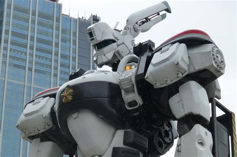 A Large White Robot Standing Next To A Tall Building