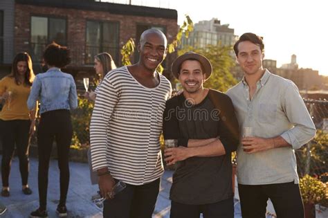 Three Male Friends At A Rooftop Party Smiling To Camera Stock Photo