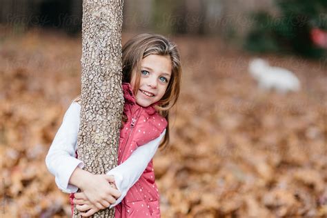 Cute Young Girl In A Vest Standing Outside Holding A Tree By Stocksy