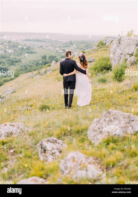 The Back View Of The Hugging Newlywed Couple Walking In The Mountains