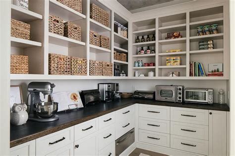 This farmhouse pantry features white shaker style cabinetry and quartz countertops. A dark stained oak countertop contrasts off-white shaker ...