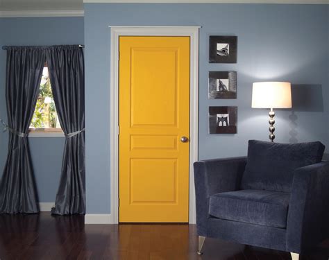 Bright Yellow Door Grey Corner Chair Some Picture Frames A Standing Lamp Grey Window Curtains With Tied Ribbon Darker Stained Wood Planks Flooring 