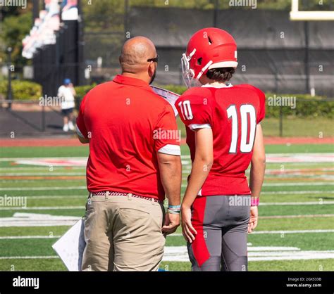 Rear View Of A High School Head Football Coach Going Over The Next Play With His Quarterback On