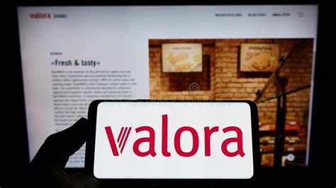 Person Holding Smartphone With Logo Of Swiss Retail Company Valora