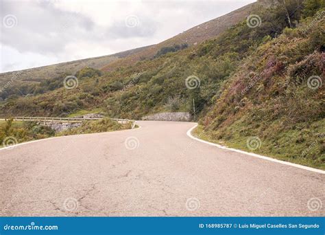 Winding Mountain Road Between Green Fields And Under Autumn Clouds