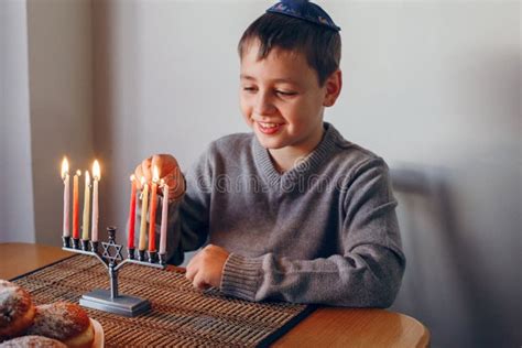 Boy In Kippah Lighting Candles On A Menorah For Traditional Winter