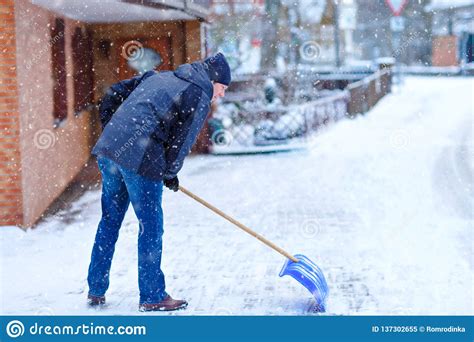 Man With Snow Shovel Cleans Sidewalks In Winter During Snowfall Winter