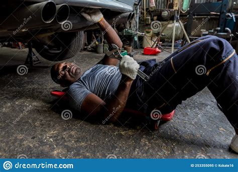 Mechanic Lying Down And Working Under Car At Auto Service Garage