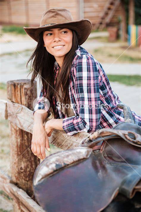 Smiling Brunette Young Woman Cowgirl Leaning On Fence In Village And