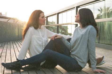 Two Young Girlfriends Sitting Together And Talking In Outdoors By