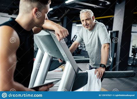 Senior Sportsman Running On Treadmill With Trainer In Gym Stock Image