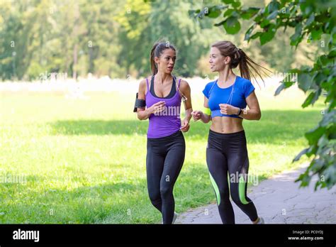 two beautiful and attractive fitness girls are jogging in the park on a sunny morning stock