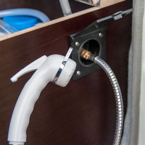 A White Hose Connected To An Outlet In A Wooden Cabinet With Other Items On The Shelf