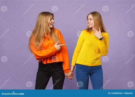 Two Young Blonde Twins Sisters Girls In Vivid Clothes Holding Hands Pointing Index Finger At