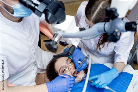 Dentist With Assistant Under Microscope Treats The Patients Teeth