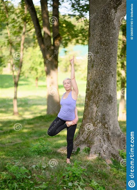 A Middle Aged Woman Practices Yoga Outdoors In The Vrikshasana Pose