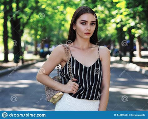 Young Girl Model Posing At The Park Looking At Camera And Keeping A Bag