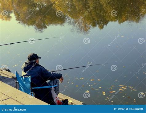 Fisherman With Fishing Rods Catches Fish In A River Sitting On The