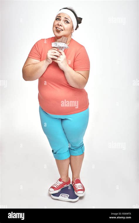 Amusing Chubby Woman Is Eating Chocolate While Standing On The Scales