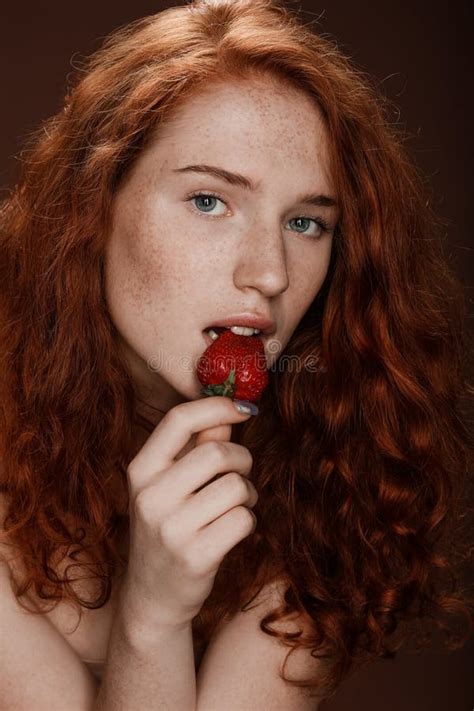 Sensual Redhead Woman Eating Fresh Strawberry On Brown Stock Image
