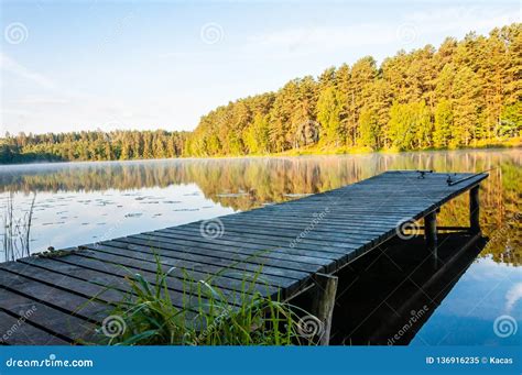 Fishing Rods Lying On A Wooden Pier On Lake With Evergreen Forest On