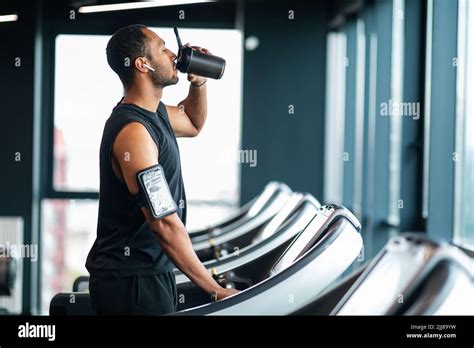 Handsome Black Male Athlete Drinking Water While Training At Treadmill