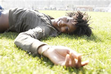 Young African American Woman Laying Down On Green Grass In The City On