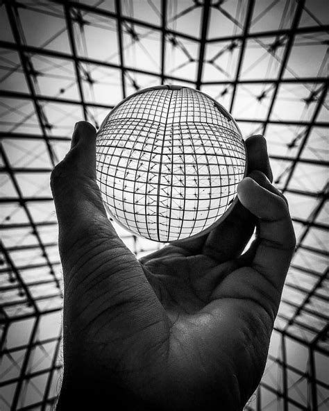 A Person Holding Up A Glass Ball In Front Of A Ceiling With Lines On It