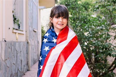 Blackhaired Girl Covered With A Large American Flag In The Garden Of