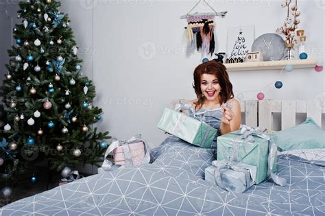 chica desnuda acostada en la cama cubriendo contra el árbol de año nuevo con cajas de regalos en