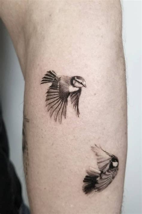 A Small Black And White Bird Tattoo On The Right Arm With Two Smaller