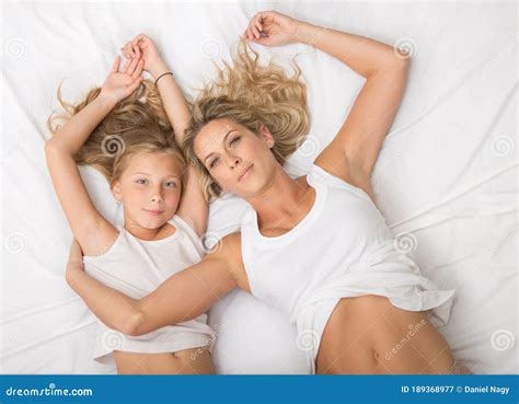 beautiful blonde smiling mother and daughter lay on bed together on white blanket from above