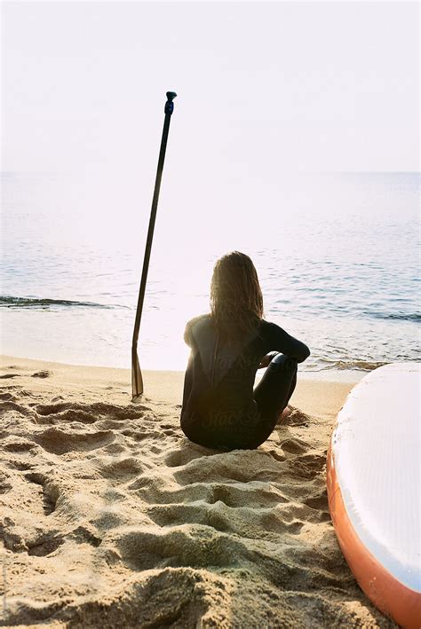 Woman In Wetsuit Sitting On Seashore With Paddle By Stocksy