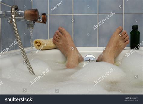 A Man S Feet Poking Out Of A Bubble Bath With Water Running In To The Side A Loofah And