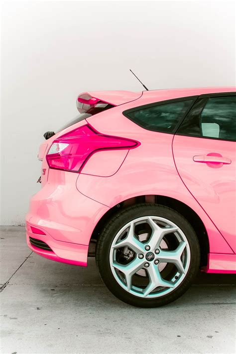 A Pink Car Parked In A Garage Next To A White Wall And Black Rims