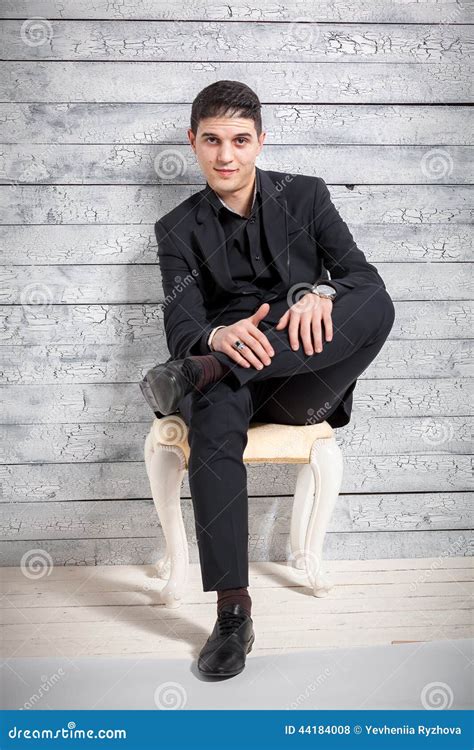 Man In Suit Sitting On Chair With Legs Crossed At Studio Stock Photo