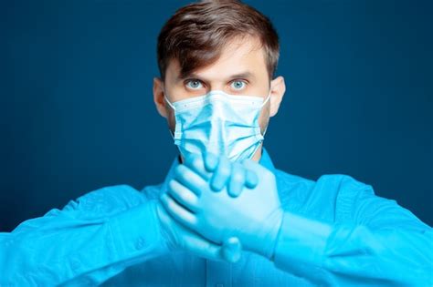 premium photo doctor in a medical mask and gloves in a blue uniform gestures with his hands