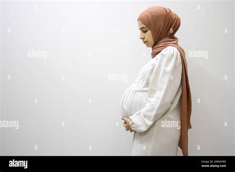 pregnant arabic muslim female on isolated white background touching her tummy showing her body