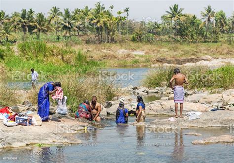 Women And Men Bathe And Wash Clothes In A River Near An Indian Village